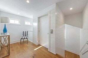 A modern interior with a wooden floor, a striped chair, a white door, and a blue lamp on a table. - A Shore Thing: On Canal! Pool Spa!  Rooftop Deck by Anna Maria Life Vacation Rentals (Anna Maria)