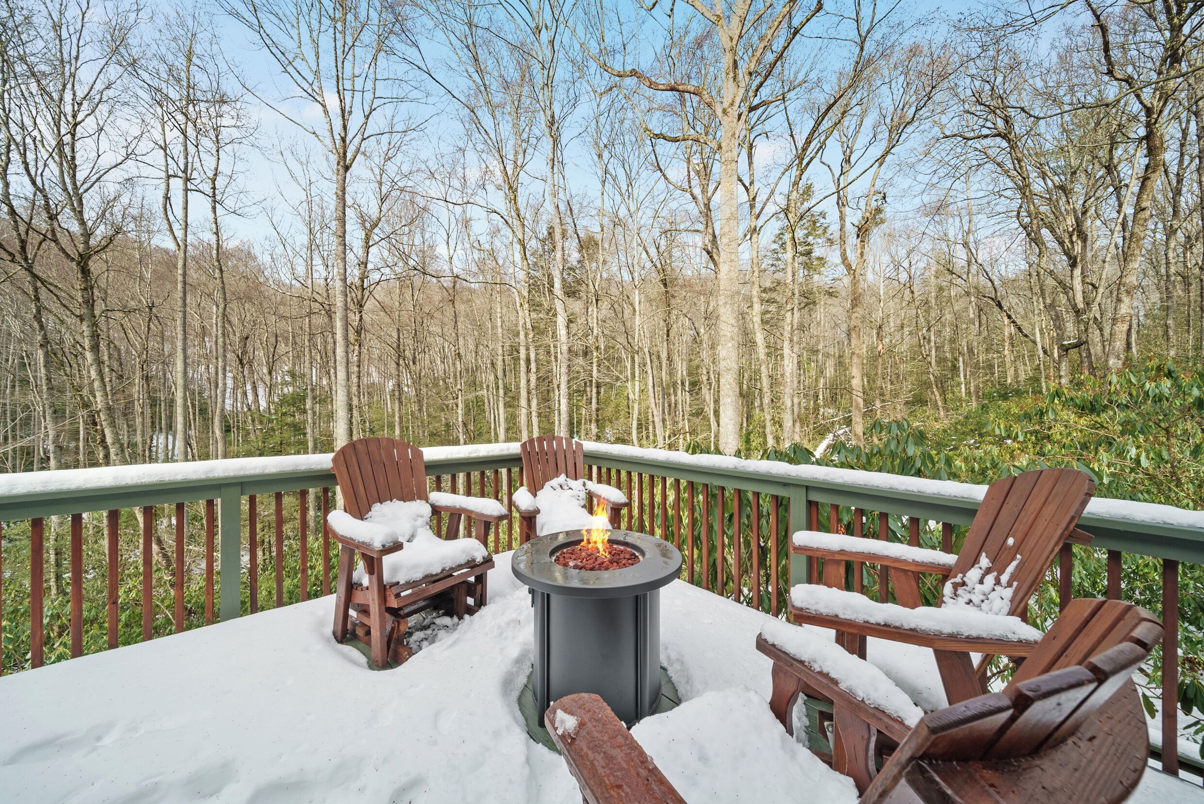Une terrasse avec un foyer entouré de chaises en bois, de la neige au sol et une forêt en arrière-plan.