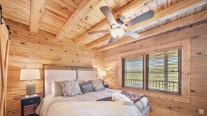 Ein Schlafzimmer einer Holzhütte mit einem Bett, einem Nachttisch, einer Lampe und einem Deckenventilator.