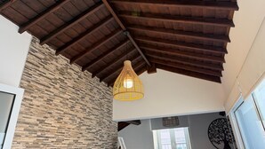 Una habitación con techo de madera inclinada, una lámpara de fibra y una pared de piedra.