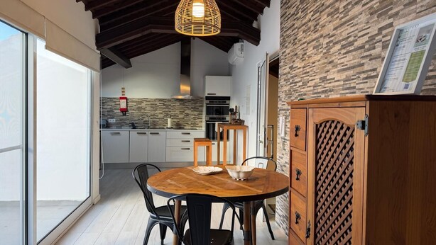 Una cocina moderna con protector contra salpicaduras de piedra, un comedor con mesa y sillas de madera, y una lámpara colgante.