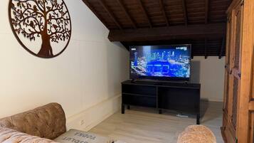 Una sala de estar con una televisión mostrando un paisaje urbano, techo de madera y un adorno mural con forma de árbol.