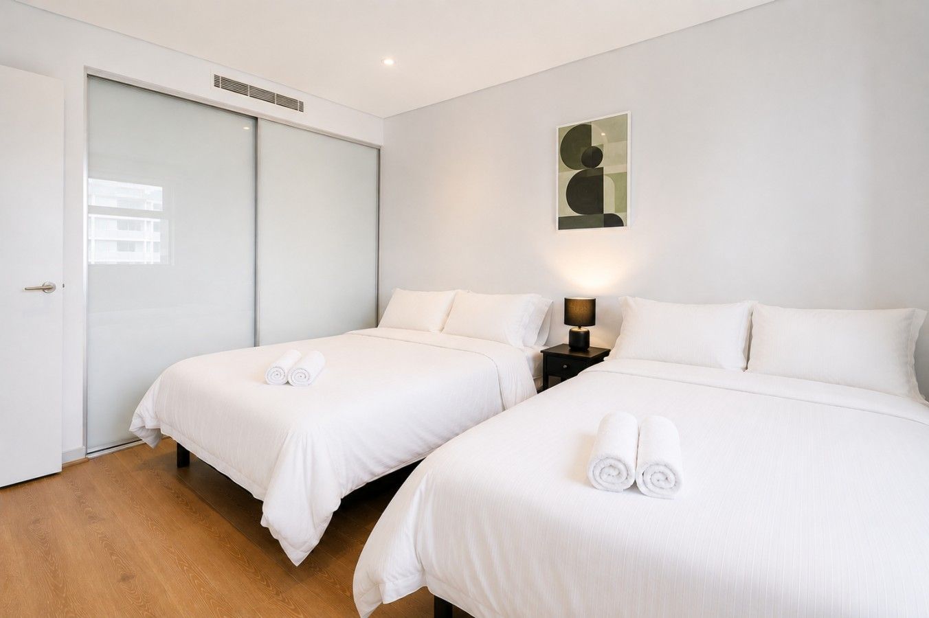 Een hotelkamer met twee bedden, een schuifdeur, een wanddecoratie en een nachtkastje met een lamp.