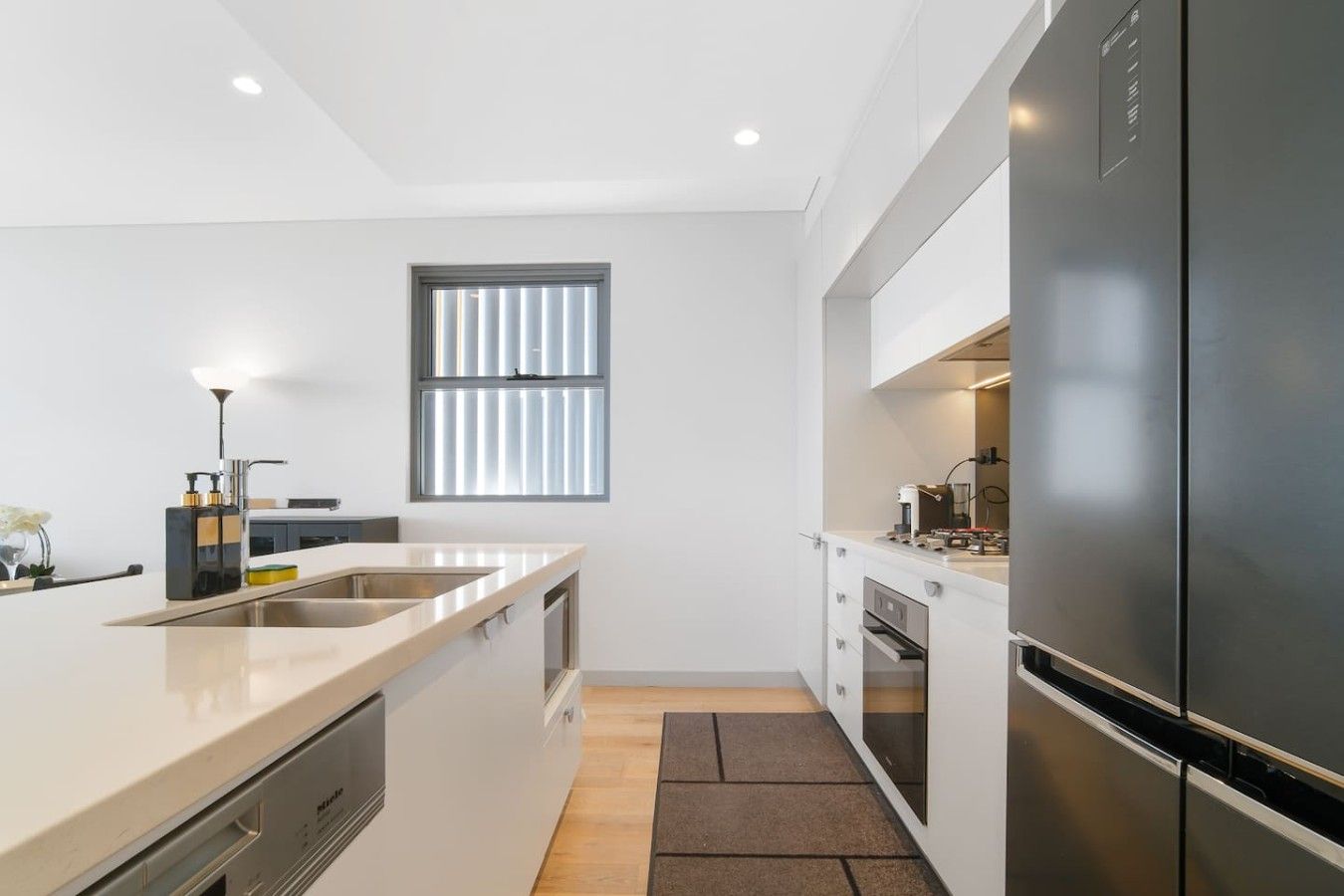 Een moderne keuken met een grote koelkast, een raam met zonwering en een aanrecht met een spoelbak.