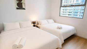 Een hotelkamer met twee bedden, een nachtkastje, een lamp, een schilderij en een raam met uitzicht op gebouwen.