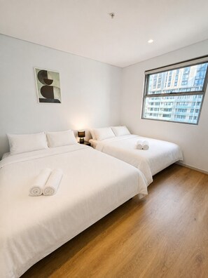 Een hotelkamer met twee bedden, een nachtkastje, een lamp, een schilderij en een raam met uitzicht op gebouwen.