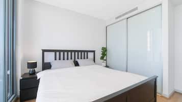 A modern bedroom with a large bed, a bedside table with a lamp, a potted plant, and a sliding closet door.