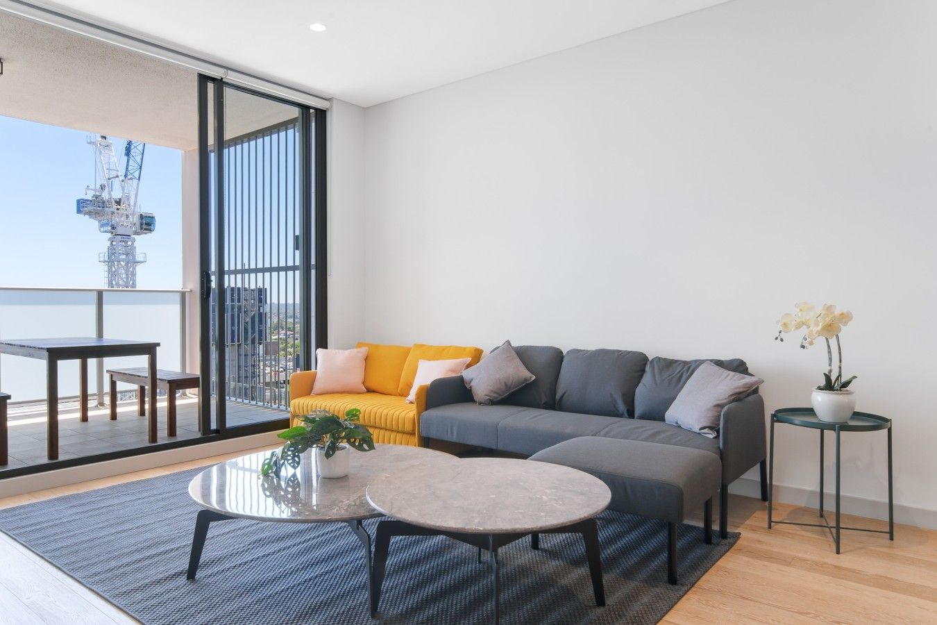A modern living room with a sofa, coffee table, and a balcony with a view of a construction site.