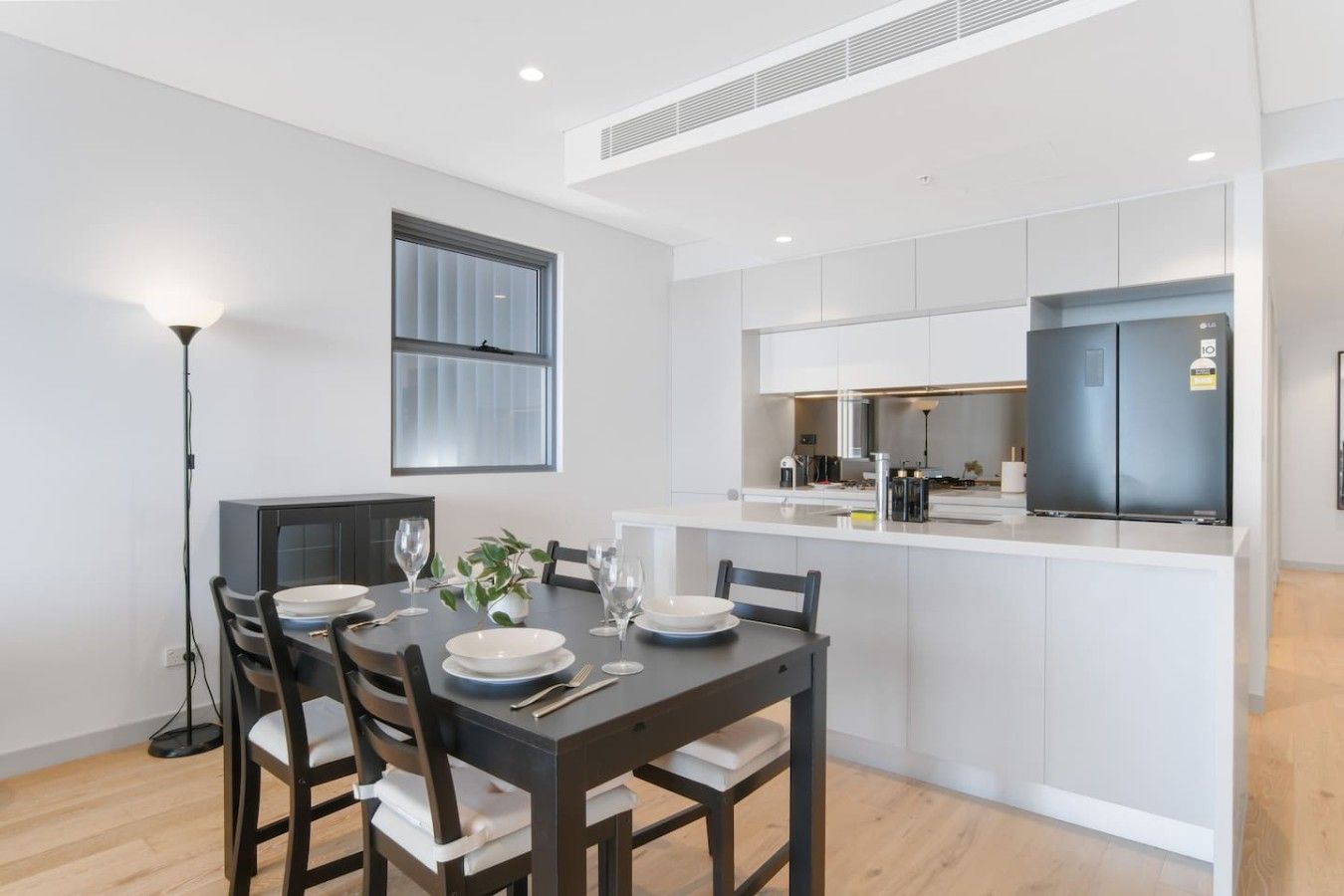 A modern kitchen with white cabinetry, a built-in oven, and a dining area with a table set for four.