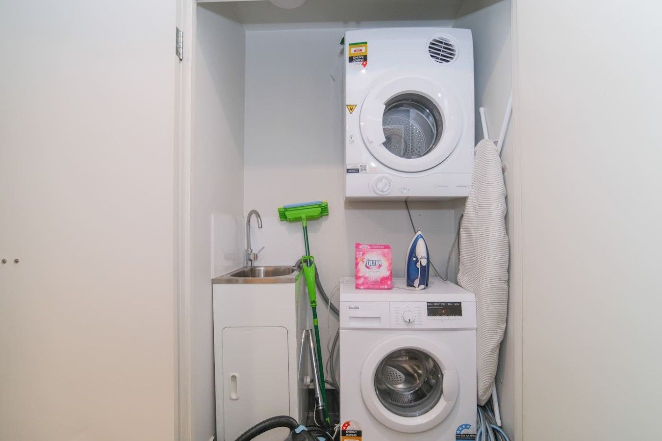 A laundry room with a washing machine, dryer, and a green mop.