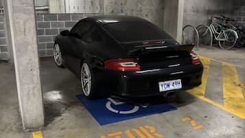 A black car parked in a visitor parking area of a building with concrete pillars and a tiled wall.