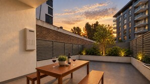 An outdoor patio with a wooden table and benches, a potted plant, and a bottle of wine.
