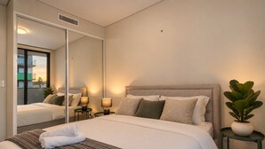 A hotel room with a large bed, bedside lamps, a mirror, and a potted plant.