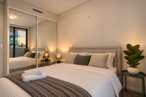 Una habitación de hotel con una cama grande, lámparas de noche, un espejo y una planta en maceta.
