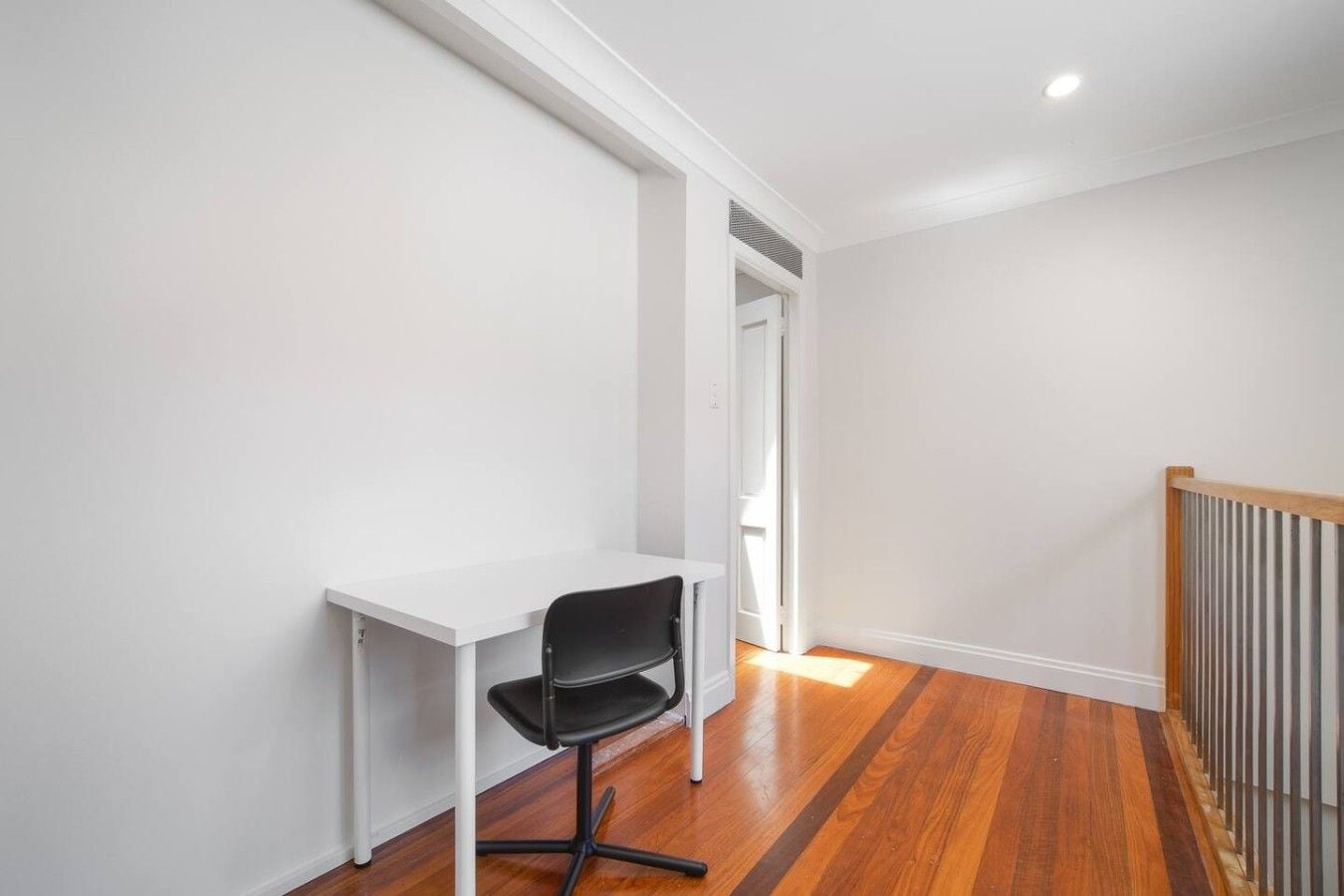A room with a white desk and black chair, wooden flooring, and a white door.