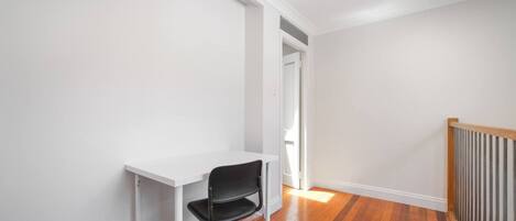 A room with a white desk and black chair, wooden flooring, and a white door.