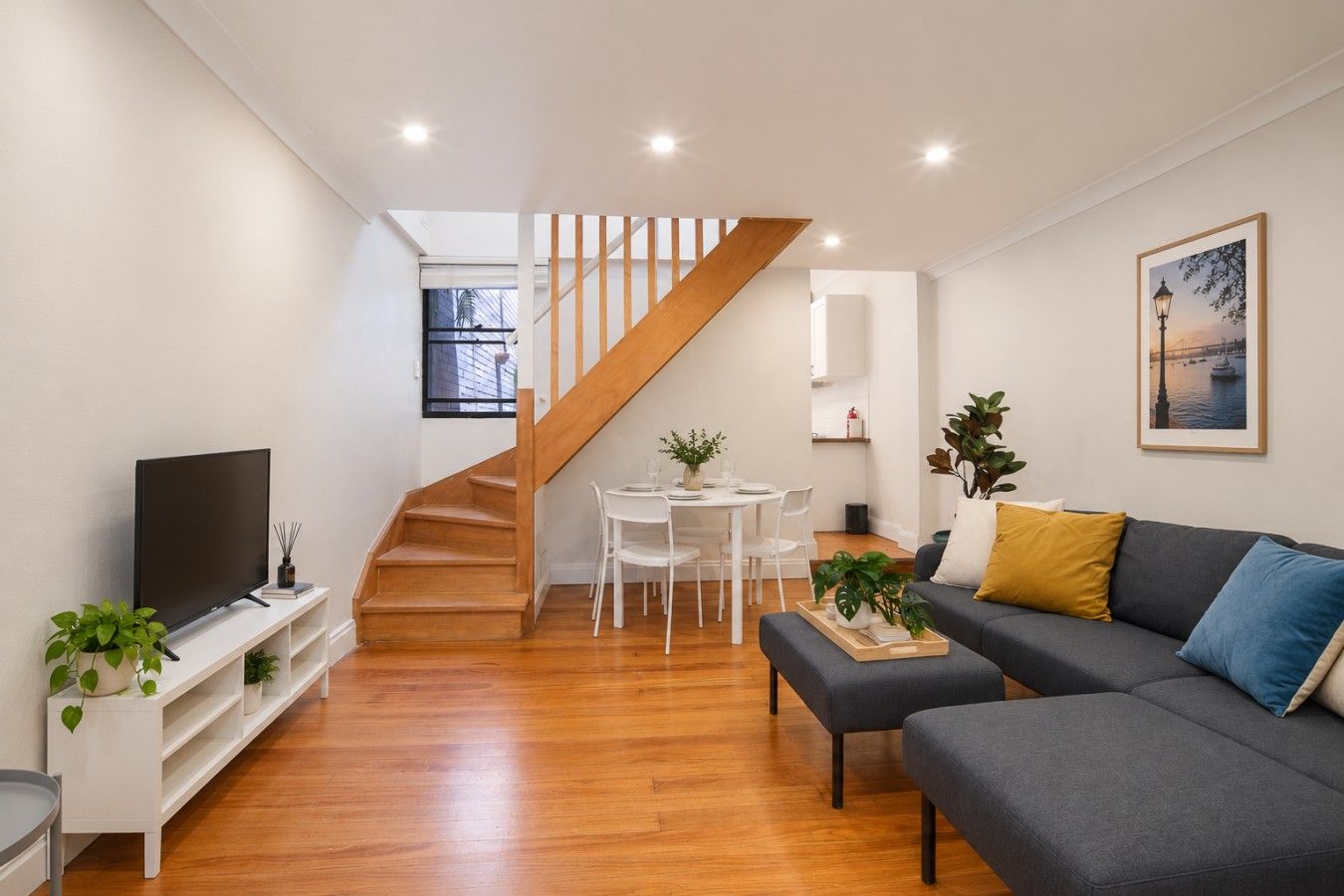A modern living room with a staircase, a flat-screen TV, a sofa, and a dining area.