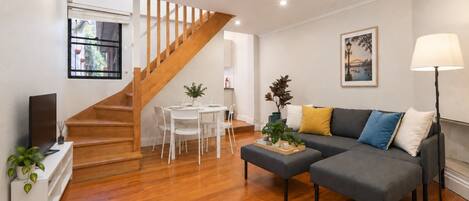 A modern living room with a staircase, a dining area, and a sofa with cushions.