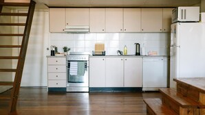 Een keuken met witte kasten, een roestvrijstalen oven, een magnetron en een vaatwasser. Er staat een houten bankje en een ladder in de hoek.