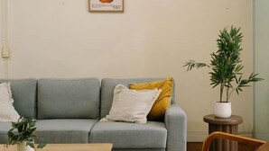 Een zithoek met een grijze bank, een houten salontafel en een bruine lederen fauteuil. Op een bijzettafeltje staat een plant in pot en aan de muur hangt een lijst met een afbeelding.