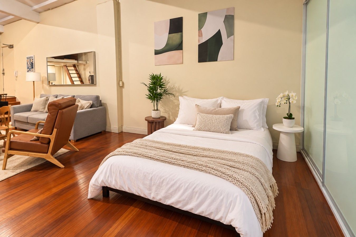 A bedroom with a large bed, a sitting area with a sofa and armchair, a small side table, and a potted plant.