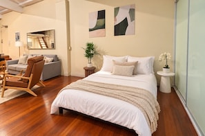 Une chambre avec un grand lit, un coin salon comprenant un canapé et un fauteuil, une petite table d’appoint et une plante en pot.