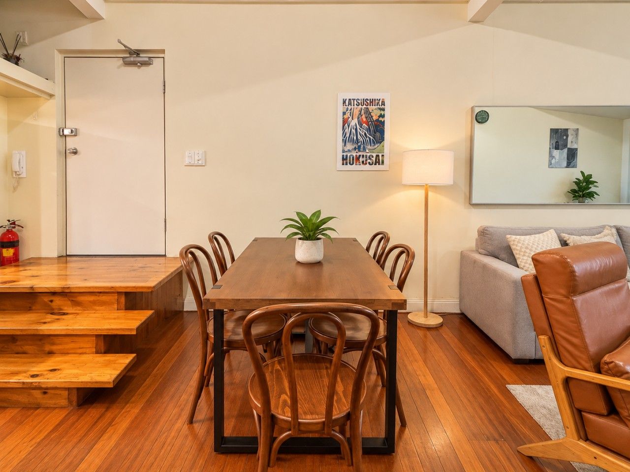 A dining area with a wooden table and chairs, a potted plant, and a sofa with cushions.