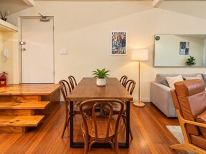 Een eetgedeelte met een houten tafel en stoelen, een plant in pot en een bank met kussens.
