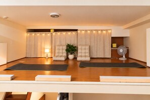 Une pièce comprenant deux tapis de yoga, une chaise, une plante en pot et un ventilateur sur pied.