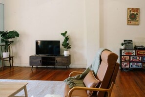 Een woonkamer met een flatscreen televisie op een houten kast, een leren fauteuil, een bijzettafeltje en een plant.