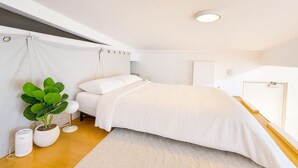 Een moderne slaapkamer met een bed, een potplant, een nachtkastje en een plafondlamp.