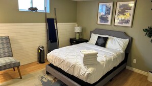 Un dormitorio con cama, mesitas de noche, una silla, un ventanal y cuadros en la pared.