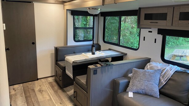 Ein kompaktes Wohnmobil-Interieur mit einer Küchenzeile, einer Sitzecke und Fenstern mit Blick auf Grünflächen.