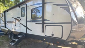 Ein weißer Wohnmobil mit Rampe, Generator und überdachtem Stauraum.