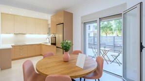 Una cocina moderna con armarios color crema, una isla central con un jarrón rosa y un comedor con sillas rosas.