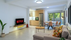 Una sala de estar moderna con un televisor de pantalla plana, un sofá, una mesa de comedor con sillas y una cocina al fondo.