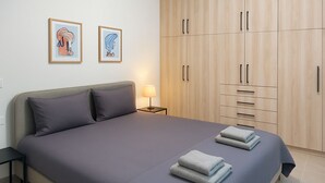 Una cama bien hecha con almohadas, una lámpara de noche y un juego de toallas dobladas. Hay dos obras de arte enmarcadas en la pared sobre la cama.