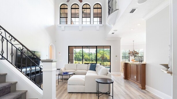 A spacious living room with a large sectional sofa, a staircase with black railings, and a view of the outdoors through large windows. - 5-Bedroom Villa in Reunion Resort, Orlando Villa 6415 (Orlando)
