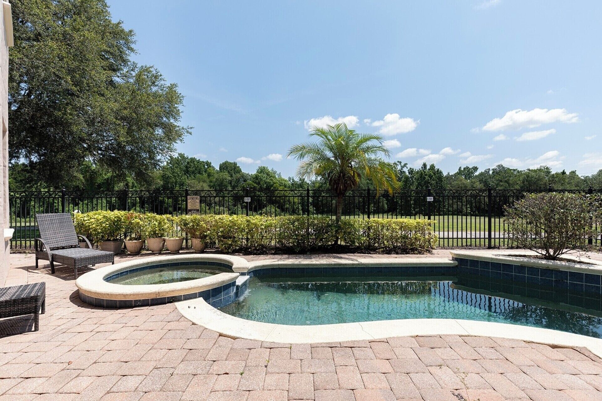 A swimming pool with a curved design, surrounded by a brick patio and outdoor furniture.
