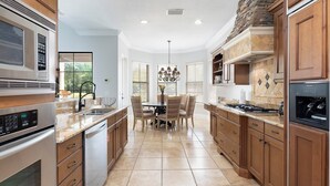 A modern kitchen with built-in appliances, wooden cabinets, and a dining area with a chandelier. - 5-Bedroom Villa in Reunion Resort, Orlando Villa 6415 (Orlando)