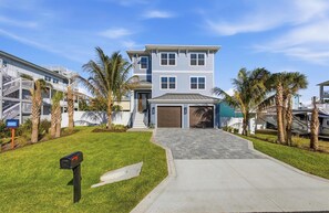 A two-story residential building with a garage, surrounded by well-maintained lawns and palm trees. - Ocean Views, Beach, Optional Heated Pool & Spa (Palm Coast)