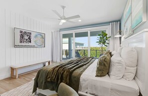 A bedroom with a bed, a ceiling fan, a large window with curtains, and a balcony. - Ocean Views, Beach, Optional Heated Pool & Spa (Palm Coast)