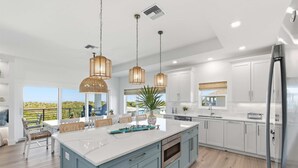 A modern kitchen with a large island, white cabinets, and pendant lighting. - Ocean Views, Beach, Optional Heated Pool & Spa (Palm Coast)