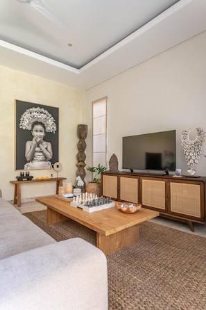 A living room with a wooden coffee table, a television, a sofa, and a painting on the wall. - Villa Athena One - Where Romance Meets Relaxation (Denpasar)