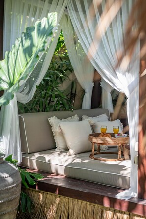 Un espace extérieur accueillant avec un canapé confortable, une table en osier sur laquelle sont disposées des boissons et un auvent qui offre de l’ombre.