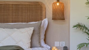 Uma cama bem arrumada com cabeceira, mesa de cabeceira com velas e luminária pendente.