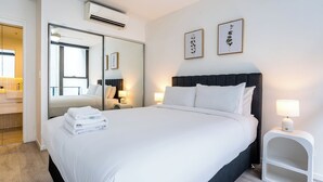 Ett hotellrum med en stor säng, en spegel, två sänglampor och inramade konstverk på väggen.