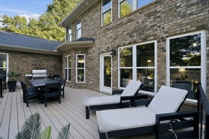 A patio with a grill, outdoor seating, and a brick house. - 3 Story Waterfront Brick Home w Brand New Pool/Spa, foosball, ping pong and much more (Mooresville)