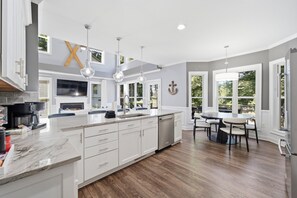 A modern kitchen with white cabinetry, a large island, and pendant lighting. - 3 Story Waterfront Brick Home w Brand New Pool/Spa, foosball, ping pong and much more (Mooresville)
