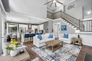 A spacious living area with a staircase, white furniture, and a kitchen in the background. - 3 Story Waterfront Brick Home w Brand New Pool/Spa, foosball, ping pong and much more (Mooresville)